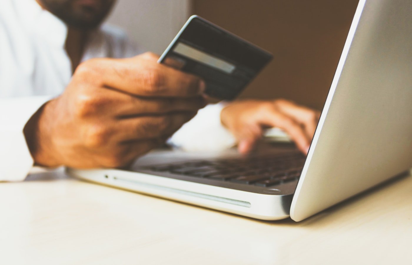 Pessoa utilizando cartão e computador em transação digital